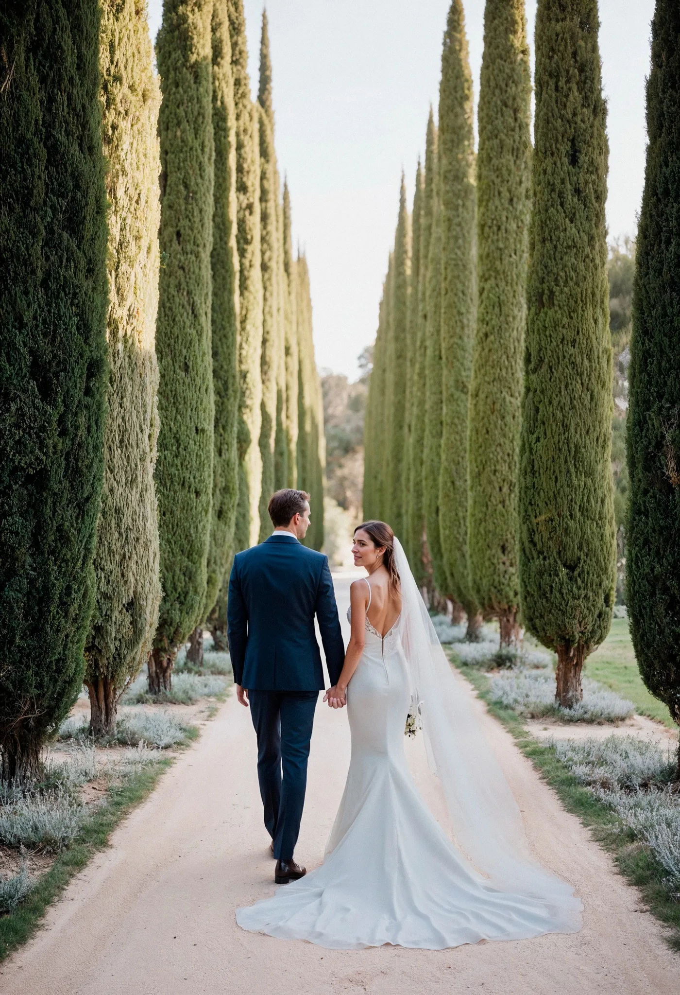 A couple walking a cypress-lined avenue after their ceremony